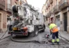 Gandia refuerza la limpieza preventiva de sus más de 9.000 imbornales ante la temporada de lluvias Operario limpiando una alcantarilla con agua a presión junto a un camión de desatascos en una calle
