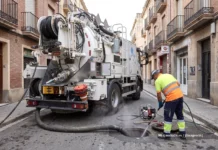 Gandia refuerza la limpieza preventiva de sus más de 9.000 imbornales ante la temporada de lluvias Operario limpiando una alcantarilla con agua a presión junto a un camión de desatascos en una calle