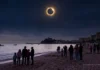 Mitos y verdades sobre el eclipse solar Personas en una playa observando un eclipse solar total sobre el mar con un castillo al fondo