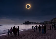 Mitos y verdades sobre el eclipse solar Personas en una playa observando un eclipse solar total sobre el mar con un castillo al fondo