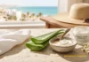 Quemaduras solares: 6 pasos eficaces para recuperar tu piel tras un día de playa Crema calmante after sun con aloe vera y pantenol junto a hojas de aloe y manzanilla frente a un paisaje costero