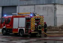 Un incendio en una nave del polígono dels Rajolars de Oliva moviliza a los bomberos de la comarca Bomberos desplegando mangueras junto a un camión para extinguir un incendio en una nave industrial