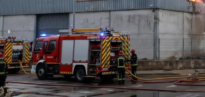 incendio en una nave Bomberos desplegando mangueras junto a un camión para extinguir un incendio en una nave industrial
